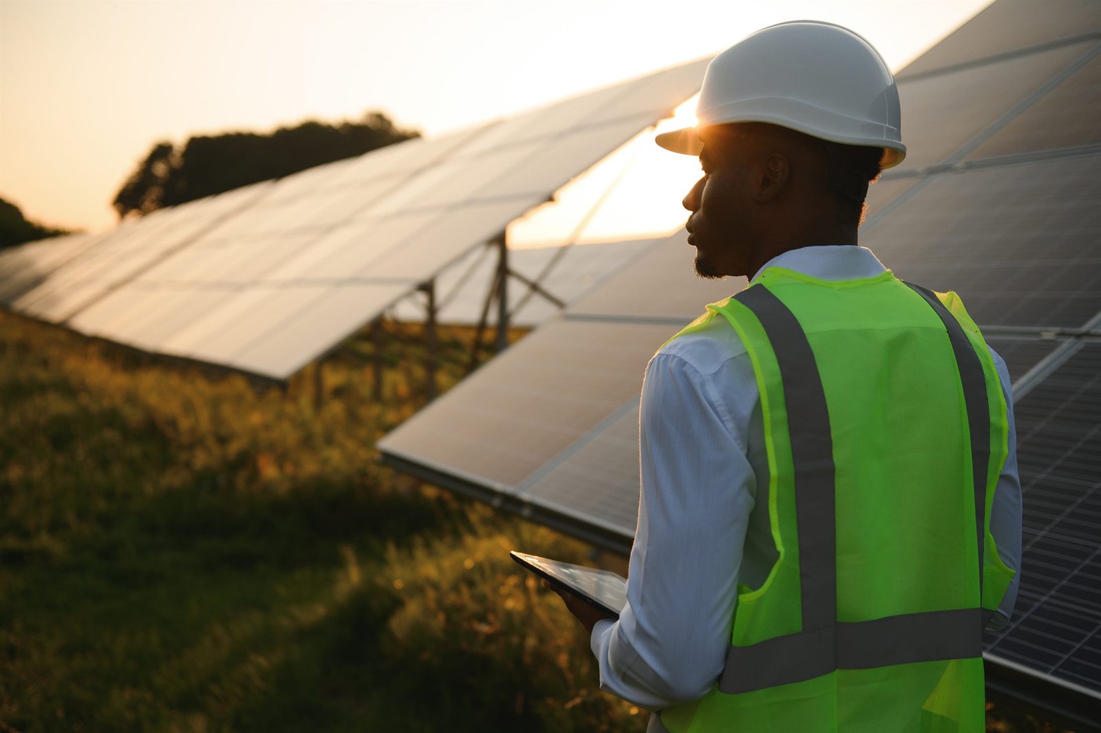 Ingeniero con chaleco de seguridad revisando un arreglo solar al atardecer